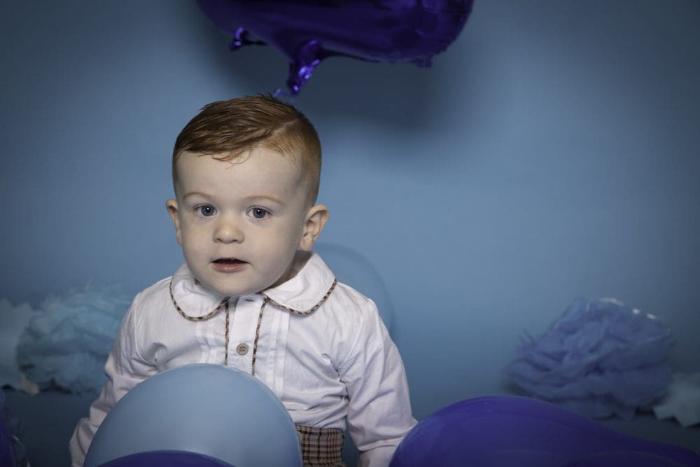 Young boy surrounded by blue and purple balloons during a studio birthday photoshoot for children in Birmingham.