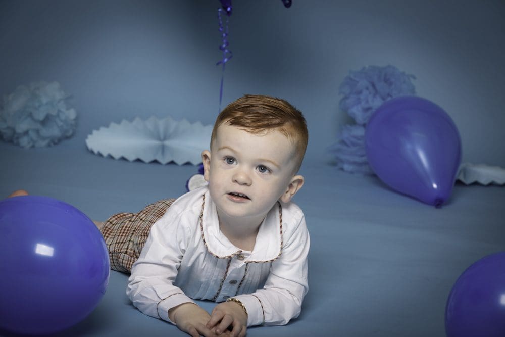Young boy lying on the floor surrounded by purple balloons during a studio birthday photoshoot for children in Birmingham.