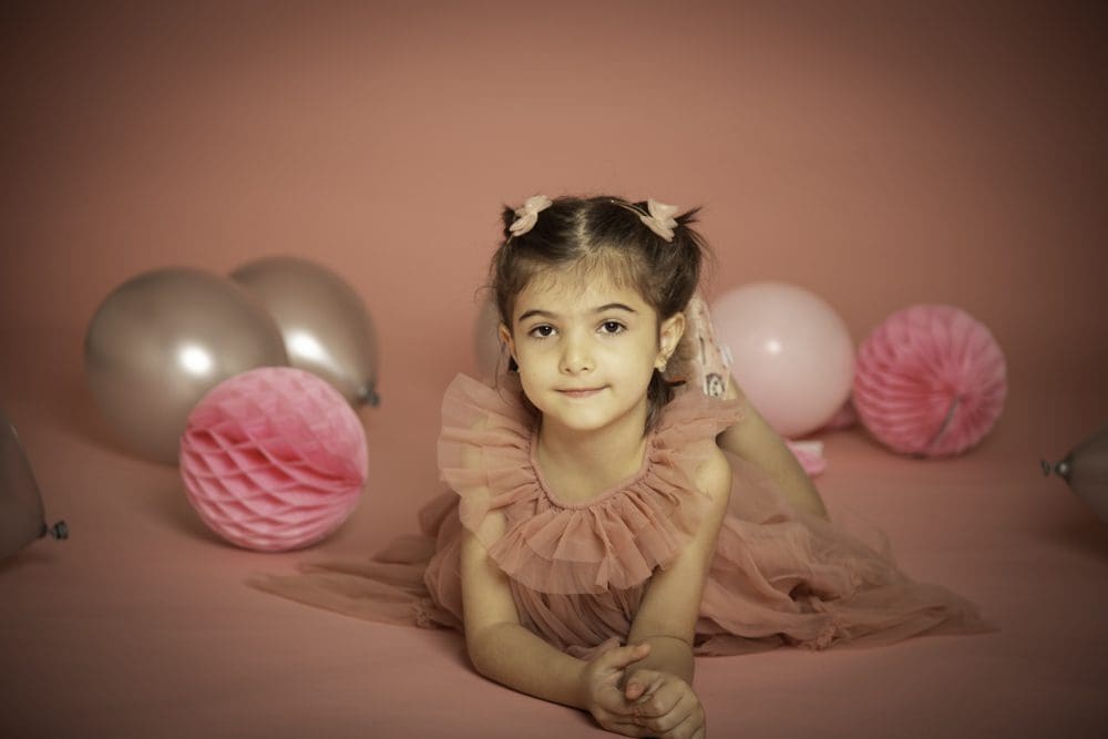 Young girl lying on the floor in a pink dress surrounded by balloons during a studio birthday photoshoot for children in Birmingham.