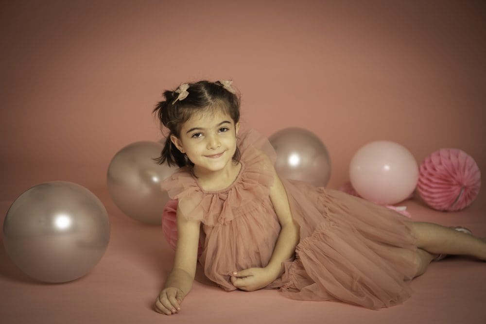 Young girl lying on the floor in a pink tulle dress surrounded by balloons during a studio birthday photoshoot for children in Birmingham.