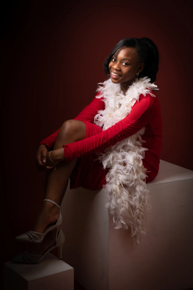 Teenage girl sitting and smiling in a red dress during a studio birthday photoshoot for children and teens in Birmingham.