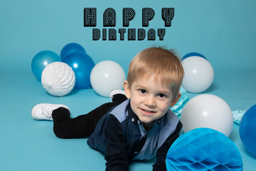 Young boy lying on the floor surrounded by blue and white balloons during a studio birthday photoshoot for children in Birmingham.