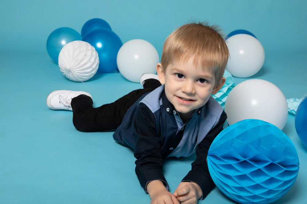 Young boy lying on the floor surrounded by blue and white balloons during a studio birthday photoshoot for children in Birmingham.