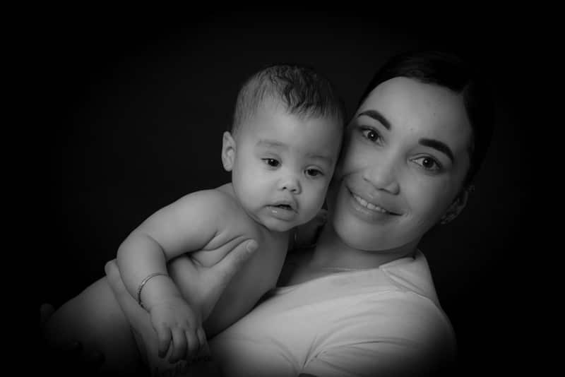 Black and white portrait of a mother holding her baby and smiling during a professional baby photoshoot in Birmingham.