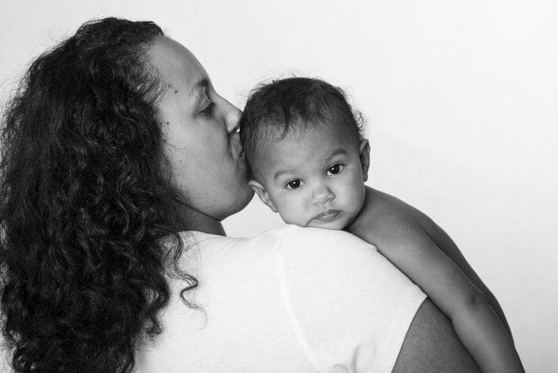 Black and white portrait of a mother kissing her baby on the head during a professional baby photoshoot in Birmingham.