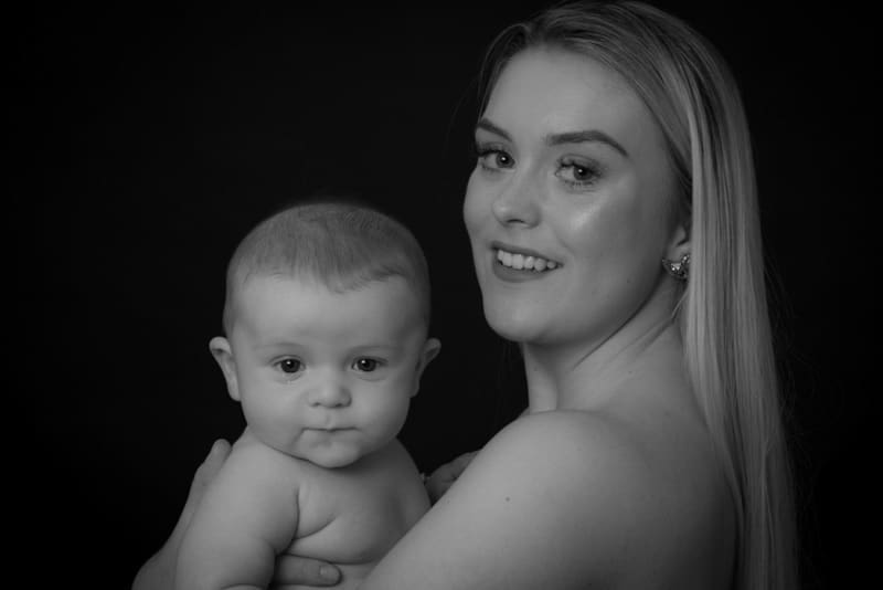 Black and white portrait of a mother holding her baby and smiling toward the camera during a professional baby photoshoot in Birmingham.