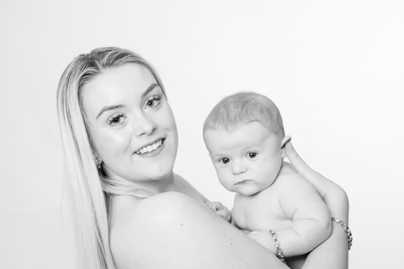 Black and white portrait of a mother holding her baby and smiling at the camera during a professional baby photoshoot in Birmingham.