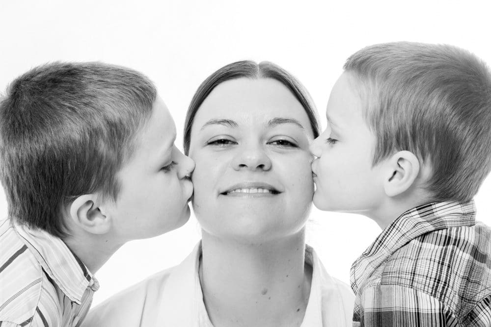 Black and white family portrait of a mum being kissed by her two children in a Birmingham studio