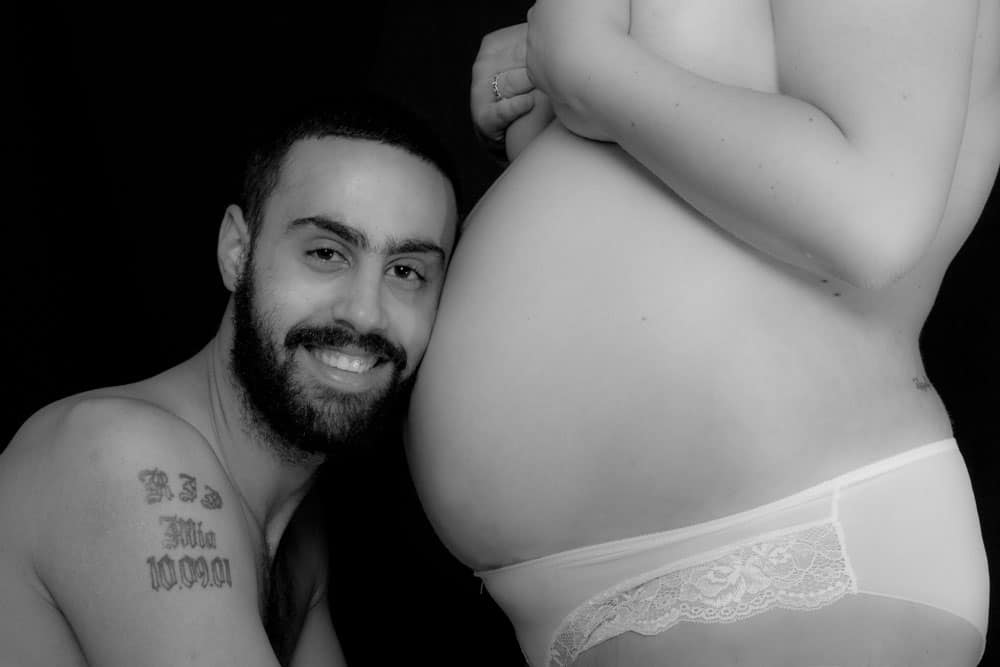 Expectant parents sharing a loving moment, with the father smiling close to the mother’s baby bump in a studio maternity photo.