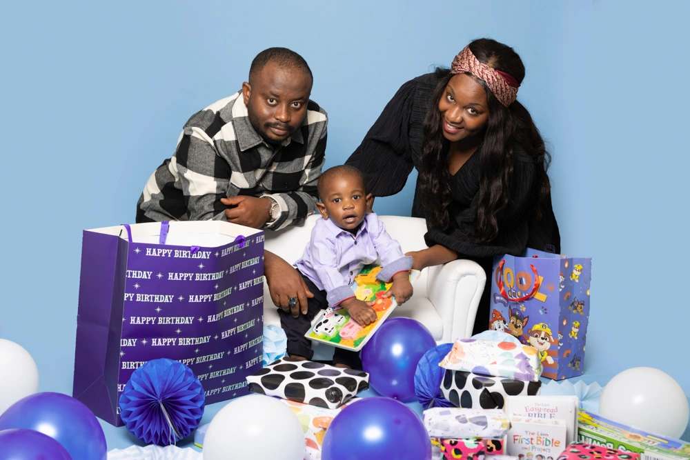 Parents sitting with their young child surrounded by birthday presents and balloons during a studio birthday photoshoot for children in Birmingham.
