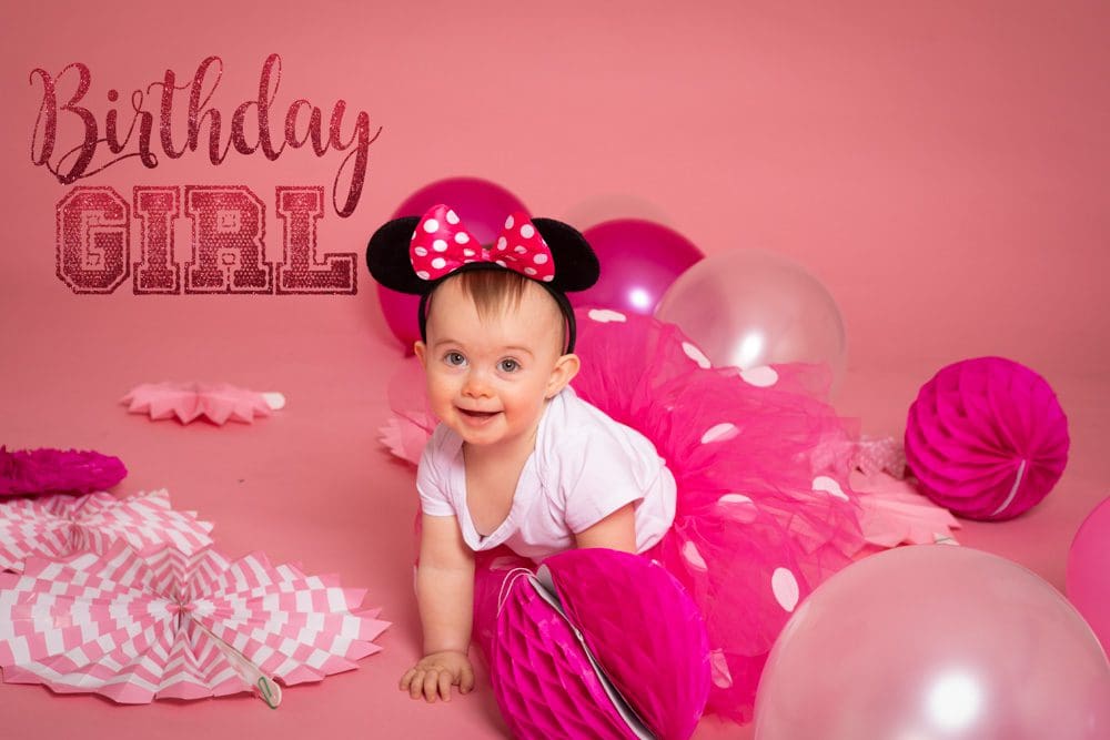 Baby girl wearing a pink tutu and Minnie Mouse ears crawling among balloons during a studio birthday photoshoot for children in Birmingham.
