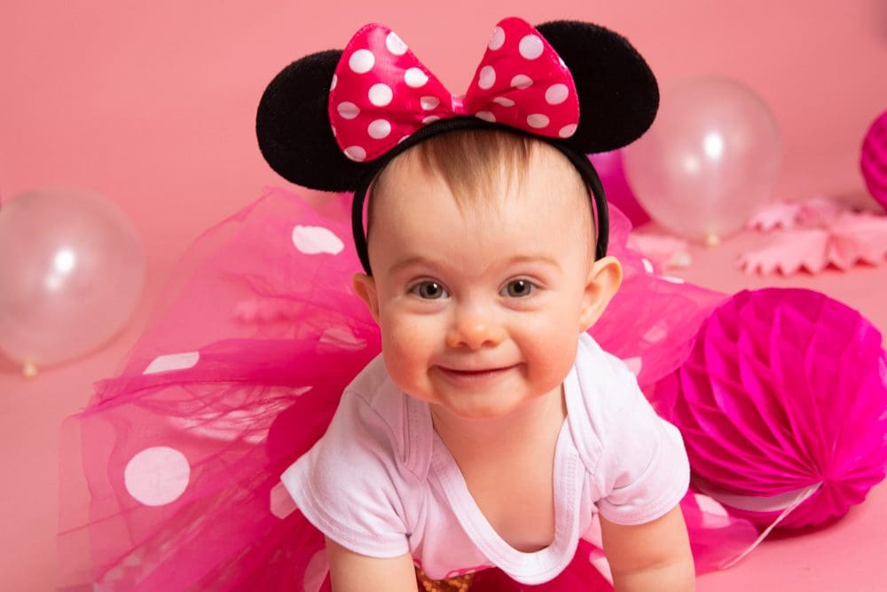 Smiling baby girl wearing Minnie Mouse ears and a pink tutu during a studio birthday photoshoot for children in Birmingham.