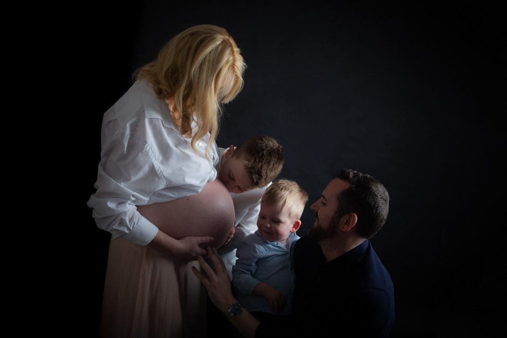 Expectant mother surrounded by her partner and children, capturing a tender family moment as they connect with her pregnancy.