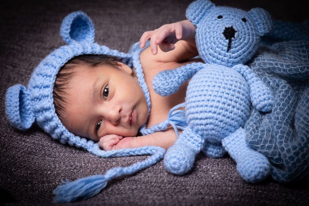 newborn baby portrait in Birmingham photography studio with blue knitted hat and teddy bear