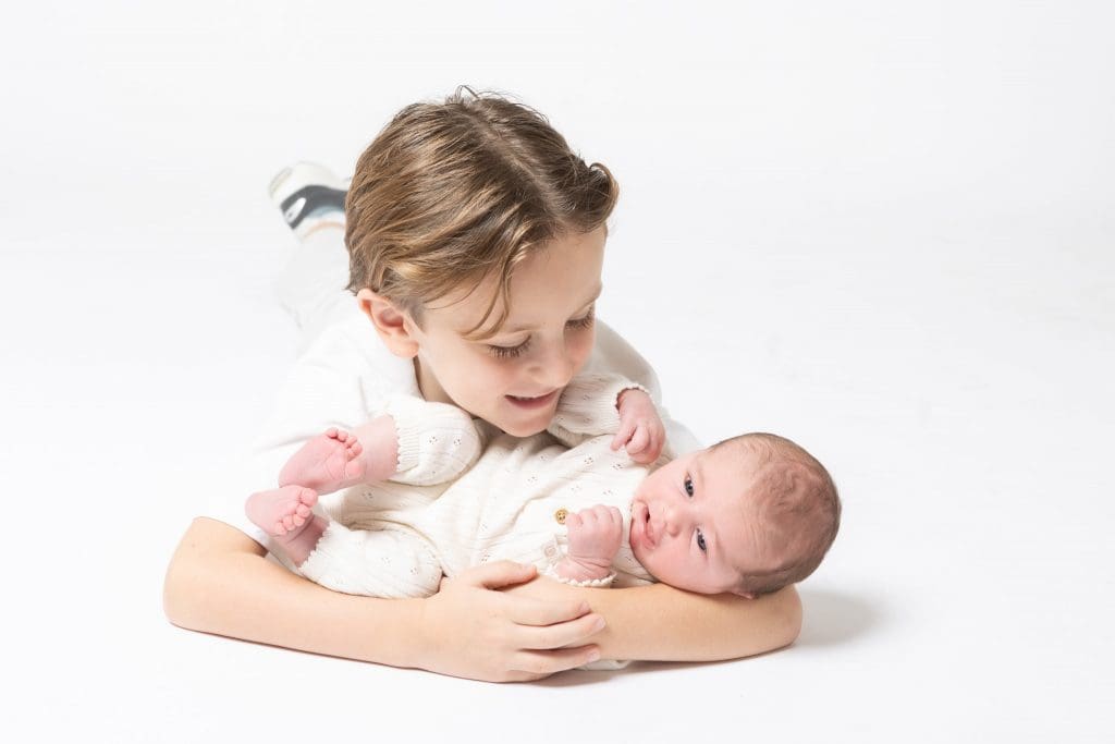 newborn baby with older sibling during Birmingham newborn photography studio session on white background